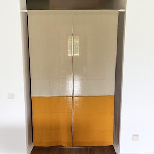 Peut inclure: Un rideau de porte à deux panneaux présentant un design bicolore avec une section supérieure beige clair et une section inférieure jaune moutarde unie. Le rideau est suspendu à une tringle à pression blanche fixée dans l'encadrement.