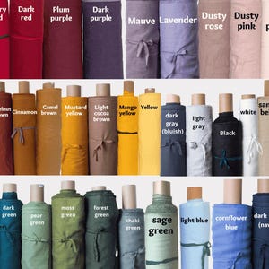 K&ouml;nnte beinhalten: Eine Sammlung von Stoffballen, angeordnet in drei Reihen, die eine gro&szlig;e Vielfalt an Farben zeigen, darunter Himbeerrosa, Koralle, Beerenrot, Pflaumenlila, Mauve, Lavendel, Altrosa, Orange, Terrakotta, Haselnuss, Senf, Gelb, Grau, Schwarz, Wei&szlig; sowie verschiedene Gr&uuml;n- und Blaut&ouml;ne.