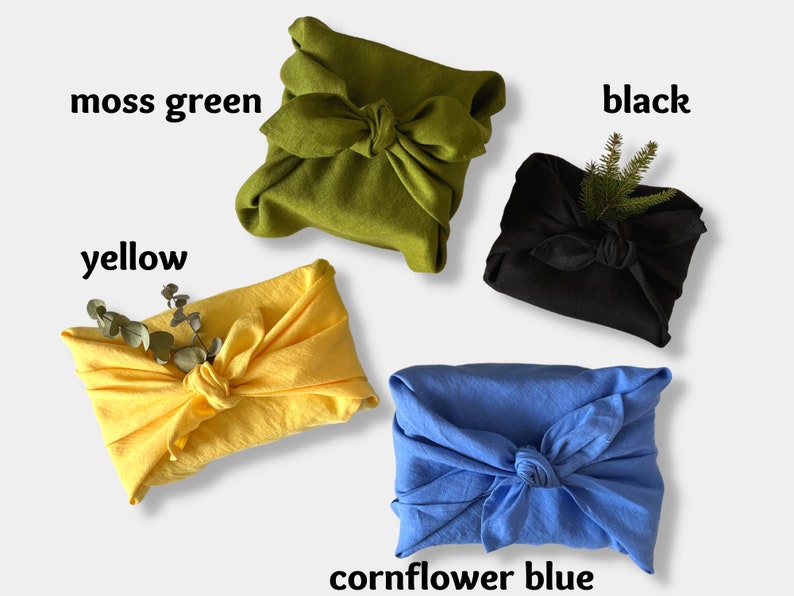 May include: Four fabric-wrapped gifts in different colors: moss green, yellow, black, and cornflower blue. Each gift is tied with a knot and decorated with a sprig of greenery.