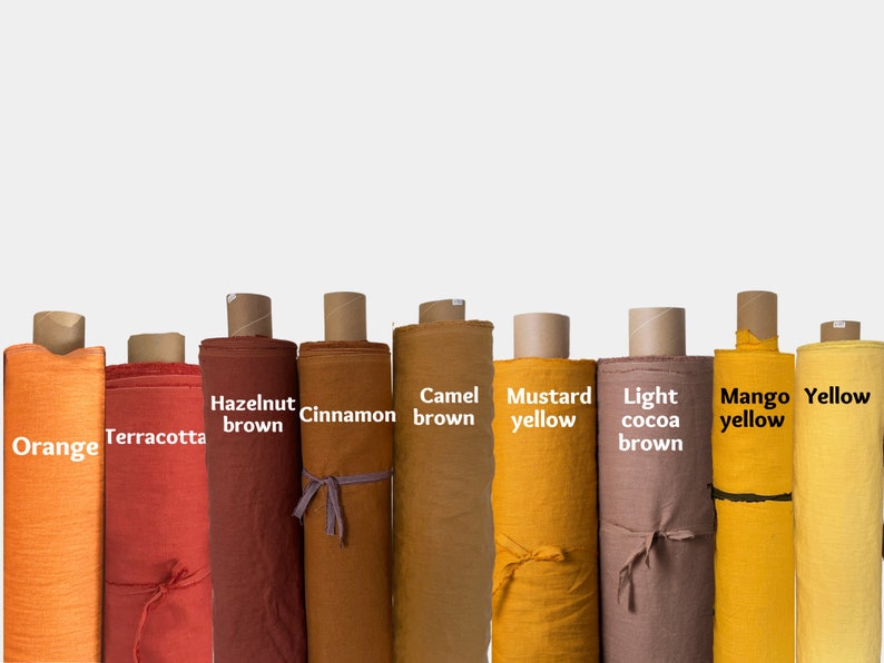 Op de afbeelding: Tien rollen stof in verschillende tinten oranje, bruin en geel. De stofrollen zijn gelabeld met de kleuren: Oranje, Terracotta, Hazelnootbruin, Kaneel, Kameelbruin, Mosterdgeel, Licht cacao bruin, Mangogeel en Geel.
