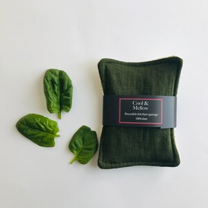 May include: A dark green reusable kitchen sponge made of 100% linen. The sponge has a label that reads "Cool & Mellow Reusable Kitchen Sponge 100% Linen".
