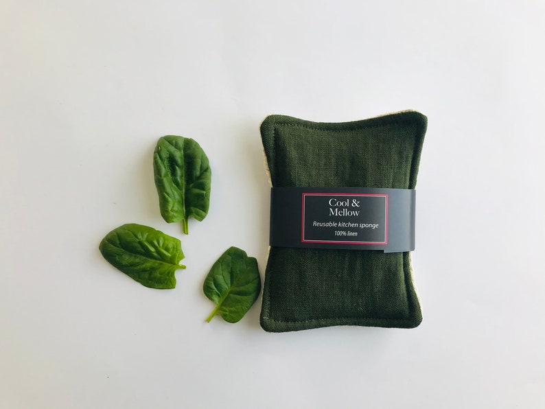 May include: A dark green reusable kitchen sponge made of 100% linen. The sponge has a label that reads "Cool & Mellow Reusable Kitchen Sponge 100% Linen".