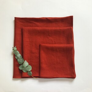 May include: Three rust-colored linen kitchen towels folded on top of each other.