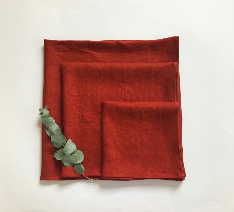 May include: Three rust-colored linen kitchen towels folded on top of each other.