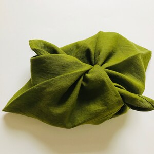 Puede incluir: Una bolsa de tela verde doblada en forma de cuadrado. La tela es texturizada y tiene un ligero brillo.