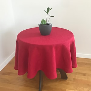 Puede incluir: Un mantel redondo rojo sobre una mesa redonda pequeña con una planta en maceta en el centro.