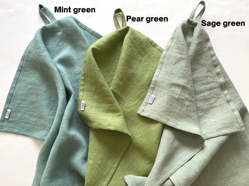 K&ouml;nnte beinhalten: Drei K&uuml;chent&uuml;cher in Minzgr&uuml;n, Birnengr&uuml;n und Salbeigr&uuml;n. Jedes Tuch hat oben eine Schlaufe zum Aufh&auml;ngen und ein kleines wei&szlig;es Markenetikett an der Seite. Der Text Mint green, Pear green und Sage green steht jeweils &uuml;ber den T&uuml;chern.