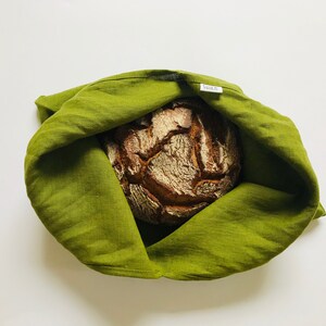Puede incluir: Una bolsa de pan de lino verde con una hogaza de pan marr&oacute;n en su interior. La bolsa tiene una peque&ntilde;a etiqueta blanca que dice "NORD".