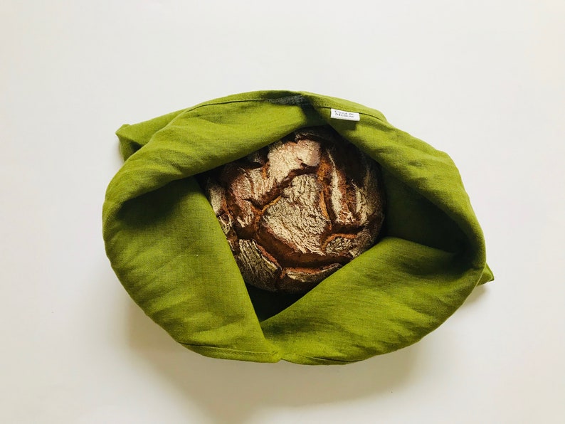 Puede incluir: Una bolsa de pan de lino verde con una hogaza de pan marr&oacute;n en su interior. La bolsa tiene una peque&ntilde;a etiqueta blanca que dice "NORD".