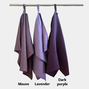 K&ouml;nnte beinhalten: Drei rechteckige K&uuml;chent&uuml;cher h&auml;ngen an einer horizontalen Metallstange. Die T&uuml;cher sind in drei verschiedenen Violettt&ouml;nen dargestellt, die von links nach rechts als Mauve, Lavender und Dark purple beschriftet sind. Jedes Tuch hat eine Schlaufe.