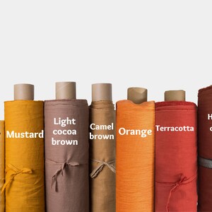 May include: Eight rolls of fabric in various shades of yellow, orange, and brown. The fabric rolls are labeled with the colors: Yellow, Mustard, Light cocoa brown, Camel brown, Orange, Terracotta, Hazelnut caramel brown.