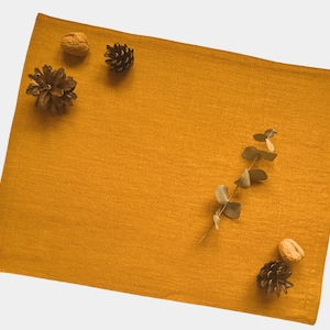 Könnte beinhalten: Ein gelber Platzdeckchen mit einem Zweig Eukalyptus, Tannenzapfen und Walnüssen.