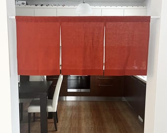 May include: A rust-coloured fabric noren curtain hanging from a white tension rod. The curtain is divided into three vertical panels of equal width, featuring a simple, solid-coloured design with a visible woven texture throughout the fabric.