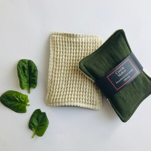 May include: Two reusable kitchen sponges. One is a beige waffle weave sponge and the other is a dark green sponge with a black label that reads "Cool & Mellow Reusable Kitchen Sponge 100% Linen".