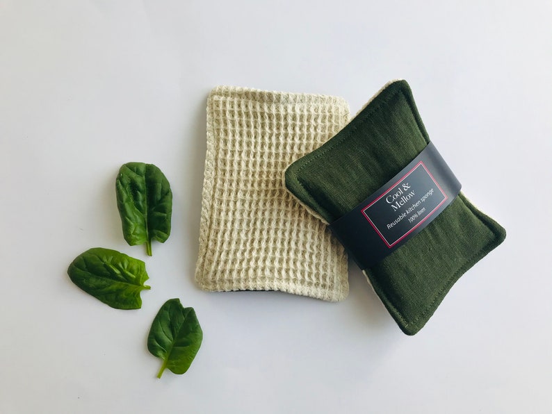 May include: Two reusable kitchen sponges. One is a beige waffle weave sponge and the other is a dark green sponge with a black label that reads "Cool & Mellow Reusable Kitchen Sponge 100% Linen".