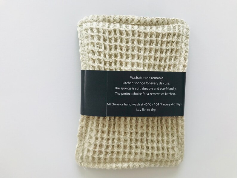 May include: A beige waffle-weave kitchen sponge with a black label that reads "Washable and reusable kitchen sponge for every day use. The sponge is soft, durable and eco-friendly. The perfect choice for a zero waste kitchen. Machine or hand wash at 40 &deg;C / 104 &deg;F every 4-5 days. Lay flat to dry."