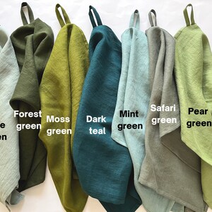 K&ouml;nnte beinhalten: Eine Sammlung von sieben K&uuml;chent&uuml;chern mit Aufh&auml;ngeschlaufen, die in einer Reihe angeordnet sind. Die Farben sind als Sage green, Forest green, Moss green, Dark teal, Mint green, Safari green und Pear green beschriftet. Jedes Tuch hat einen strukturierten Stoff.