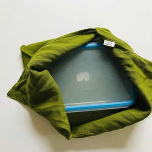 Puede incluir: Una bolsa de tela de lino verde con un recipiente de pl&aacute;stico transparente en su interior. El recipiente tiene una tapa azul y una etiqueta que dice "Cook & Modern".