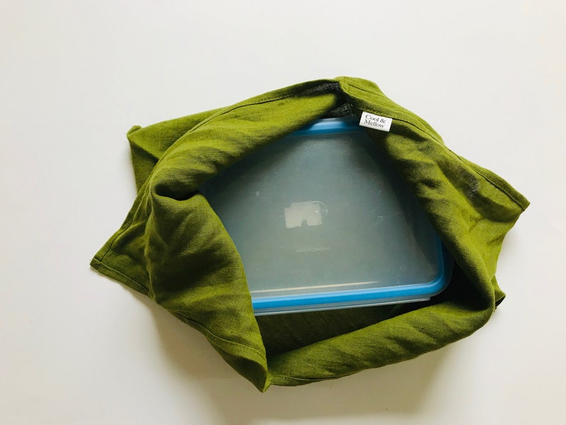 Puede incluir: Una bolsa de tela de lino verde con un recipiente de pl&aacute;stico transparente en su interior. El recipiente tiene una tapa azul y una etiqueta que dice "Cook & Modern".