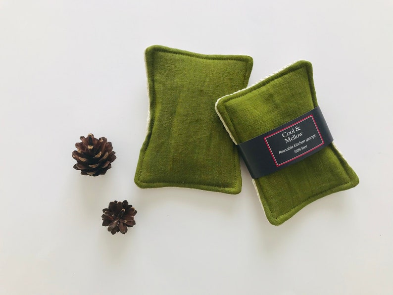 May include: Two green kitchen scrubbers with white edging. The scrubber on the right has a black label that reads "Cool & Mellow Reusable Kitchen Sponge 100% Linen".
