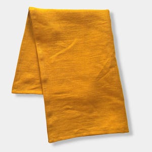 K&ouml;nnte beinhalten: Ein rechteckiges St&uuml;ck Stoff in einer einfarbigen senfgelben Farbe. Das Textil weist eine feine, gewebte Struktur mit sichtbaren horizontalen Maserungslinien und weichen Falten im gesamten Material auf, was ein schlichtes Erscheinungsbild erzeugt.