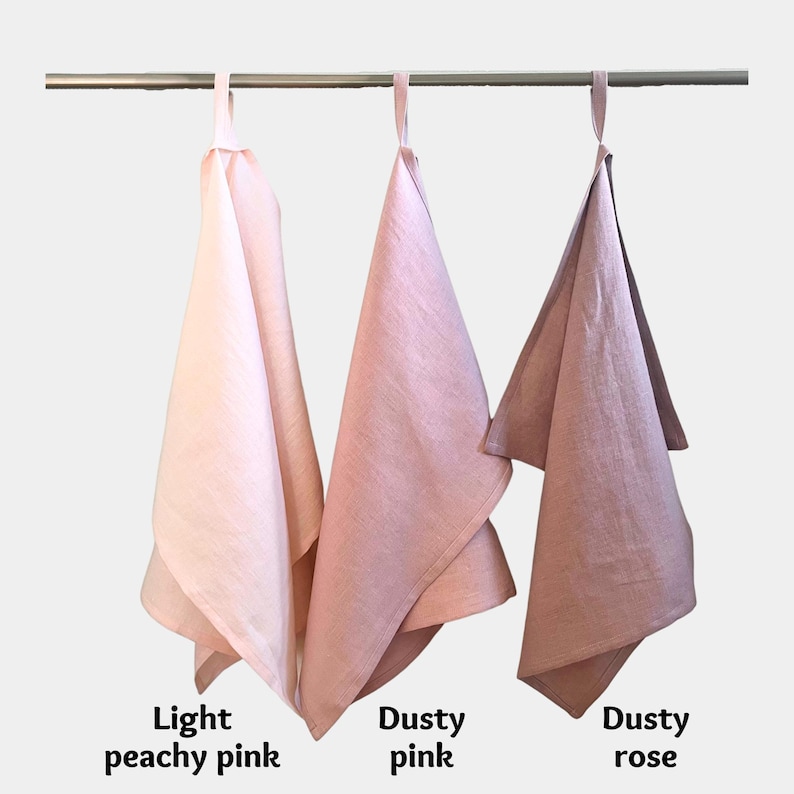 K&ouml;nnte beinhalten: Drei h&auml;ngende K&uuml;chent&uuml;cher in verschiedenen Rosat&ouml;nen, die an einer horizontalen Metallstange befestigt sind. Die T&uuml;cher sind von links nach rechts als Light peachy pink, Dusty pink und Dusty rose beschriftet und haben eine Stoffschlaufe.