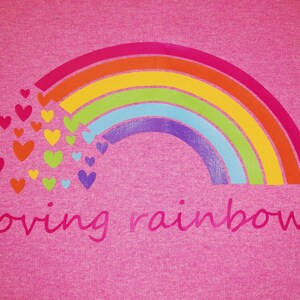 Puede incluir: Camiseta rosa con un arco&iacute;ris y corazones impresos en ella. El texto "loving rainbow" est&aacute; impreso debajo del arco&iacute;ris.