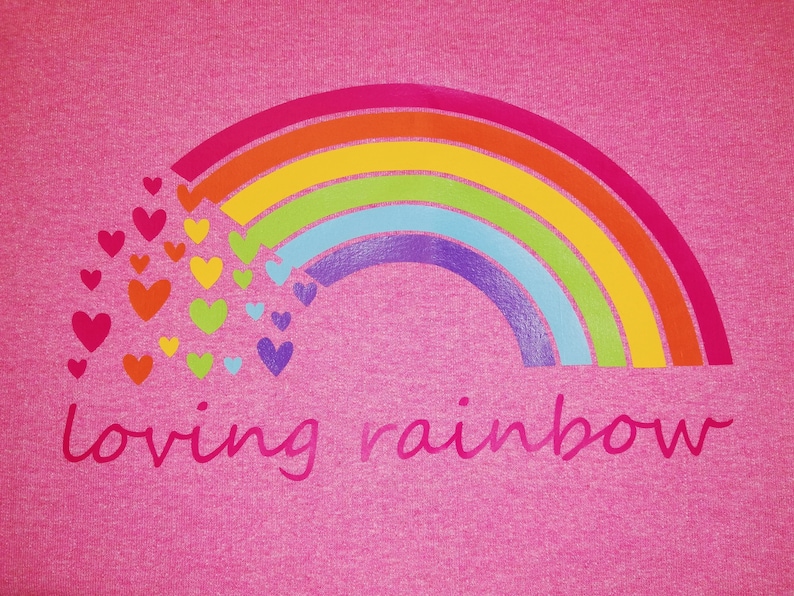Puede incluir: Camiseta rosa con un arco&iacute;ris y corazones impresos en ella. El texto "loving rainbow" est&aacute; impreso debajo del arco&iacute;ris.