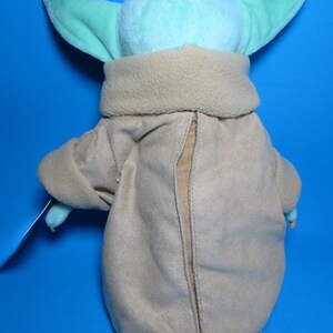 May include: A plush toy of a green character with large ears wearing a brown coat. The toy is facing away from the camera.