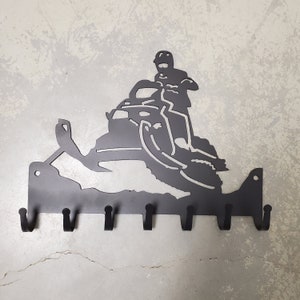 May include: Black metal snowmobile key holder with six hooks. The snowmobile is silhouetted against a white background.