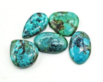 May include: Five polished turquoise gemstones in various shapes, including oval and teardrop. The stones display a mix of vibrant teal and blue hues with dark matrix patterns. The gemstones are set against a bright white background.