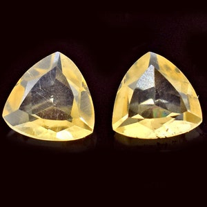 Könnte beinhalten: Zwei dreieckige, facettierte, gelbe Edelsteine mit einem leichten Orangeton. Die Edelsteine sind vor einem schwarzen Hintergrund platziert.