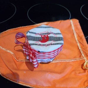 Könnte beinhalten: Ein weiß-schwarz gestreiftes Glas mit einem roten Faultier-Design und dem Text "Mamma Sloth" darauf. Das Glas ist mit einem rot-weiß karierten Band gebunden und steht auf einer orangefarbenen Stoffoberfläche.