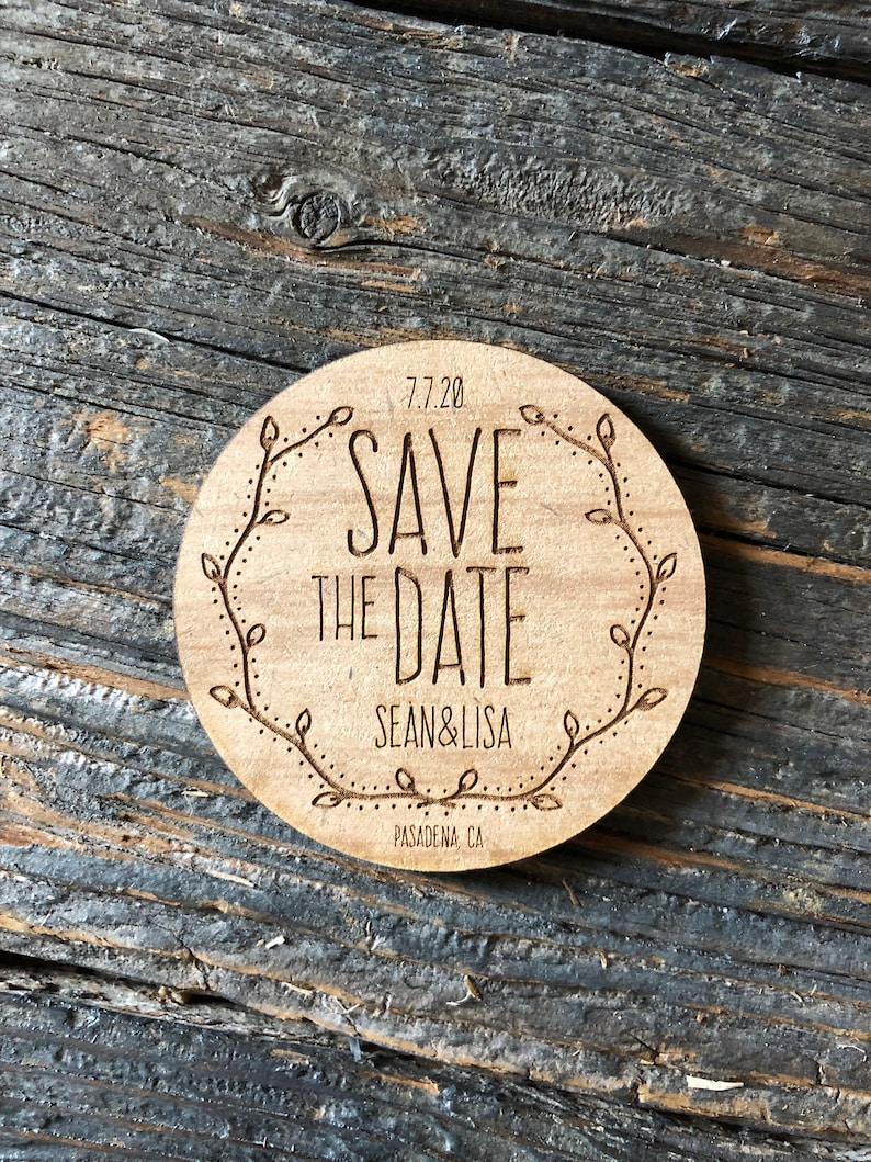 May include: A round wooden save the date card with a floral design and the text "7.7.20 Save the Date Sean & Lisa Pasadena, CA"