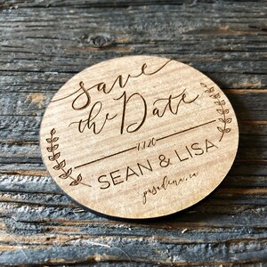 K&ouml;nnte beinhalten: Eine runde Save the Date-Ank&uuml;ndigung aus Holz. Der Text "Save the Date" ist in eleganter Schrift gehalten, mit "1.1.20" und den Namen "SEAN & LISA" darunter. Ein dekoratives Blattdesign umgibt den Text. Der Ort "pasadena.ca" ist ebenfalls enthalten.