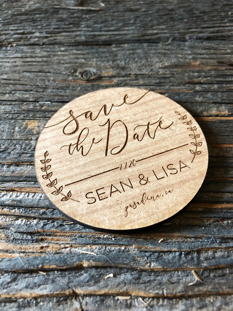 K&ouml;nnte beinhalten: Eine runde Save the Date-Ank&uuml;ndigung aus Holz. Der Text "Save the Date" ist in eleganter Schrift gehalten, mit "1.1.20" und den Namen "SEAN & LISA" darunter. Ein dekoratives Blattdesign umgibt den Text. Der Ort "pasadena.ca" ist ebenfalls enthalten.