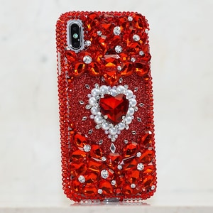 May include: Red glitter phone case with a large red rhinestone heart surrounded by white pearls. The case is covered in red rhinestones.
