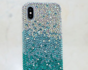 Op de afbeelding: Een transparante telefoonhoes met een verloop van iriserende witte en turquoise strass steentjes. De hoes is ontworpen voor een smartphone met een enkele camera lens.