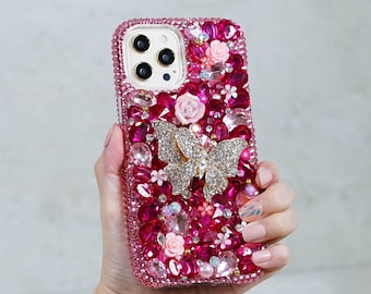 May include: A pink iPhone case featuring a butterfly design and rhinestones. The case is adorned with pink, white and gold rhinestones. The butterfly is made of gold metal and has clear wings.