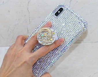 May include: A bedazzled phone case with a matching pop-up grip. The case and grip are covered in iridescent rhinestones, creating a sparkling effect. The phone case is silver and has a camera and flash.