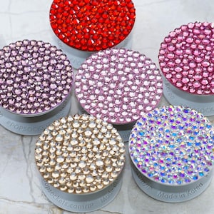 May include: Five different PopSockets phone grips with a variety of rhinestone designs. The designs include red, pink, light pink, gold, and iridescent.