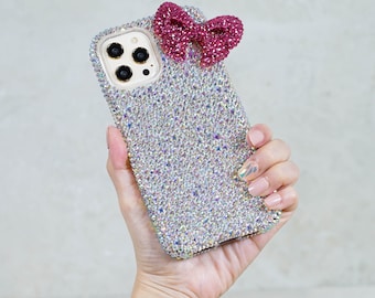Op de afbeelding: Een transparante telefoonhoes met een roze strik en strass. De hoes is ontworpen voor een iPhone.