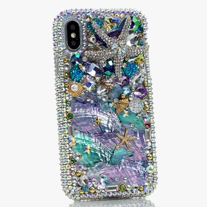 May include: A sparkly iridescent phone case with a mermaid theme. The case is covered in rhinestones, pearls, and seashells. There are two starfish, one large and one small, and a seashell with a pearl inside. The background is a swirling pattern of iridescent blue and purple.