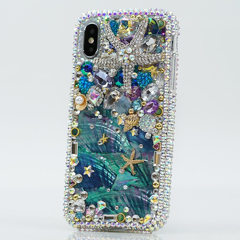 May include: A teal and blue iPhone case with a sparkly, iridescent finish. The case is decorated with rhinestones, seashells, and starfish.