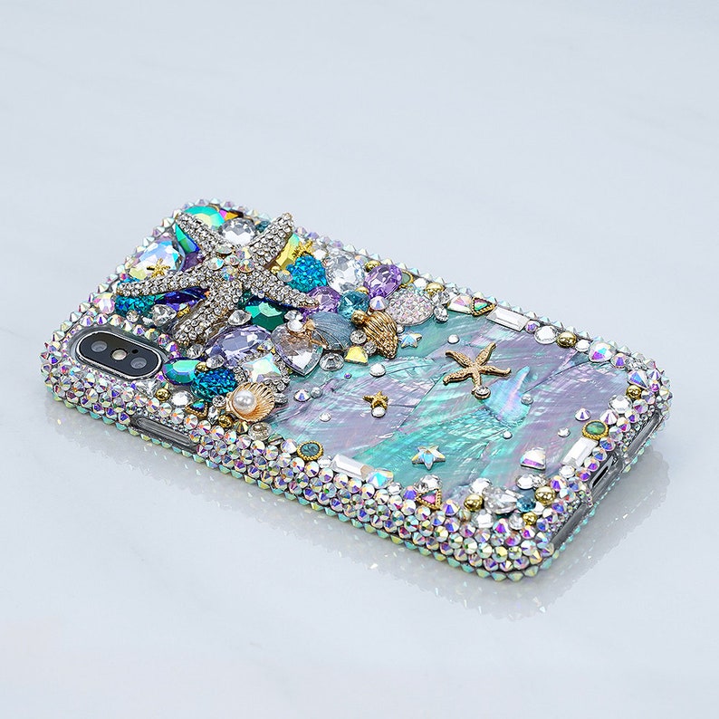 May include: A teal, iridescent, and silver iPhone case with a starfish, seashells, and rhinestones. The case has a sparkly, glittery finish.