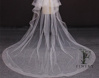 May include: A long, white tulle wedding veil with multiple layers and a scalloped edge.