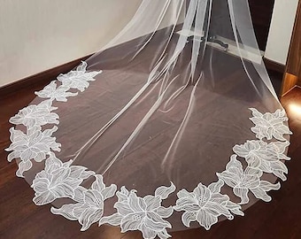 May include: A white bridal veil with a floral design around the edge. The veil is made of soft tulle and is long enough to flow behind the bride as she walks down the aisle.