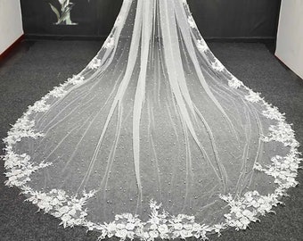 May include: A long white bridal veil with a pearl and lace trim. The veil is made of soft tulle and has a delicate floral pattern.