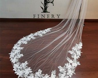 May include: A long white bridal veil with a floral lace trim. The veil is made of soft tulle and has a delicate, romantic look.