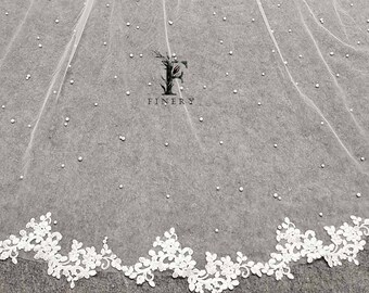 May include: White tulle wedding veil with a scalloped lace trim and scattered pearl embellishments. The veil features the word "FINERY" in a stylized font.